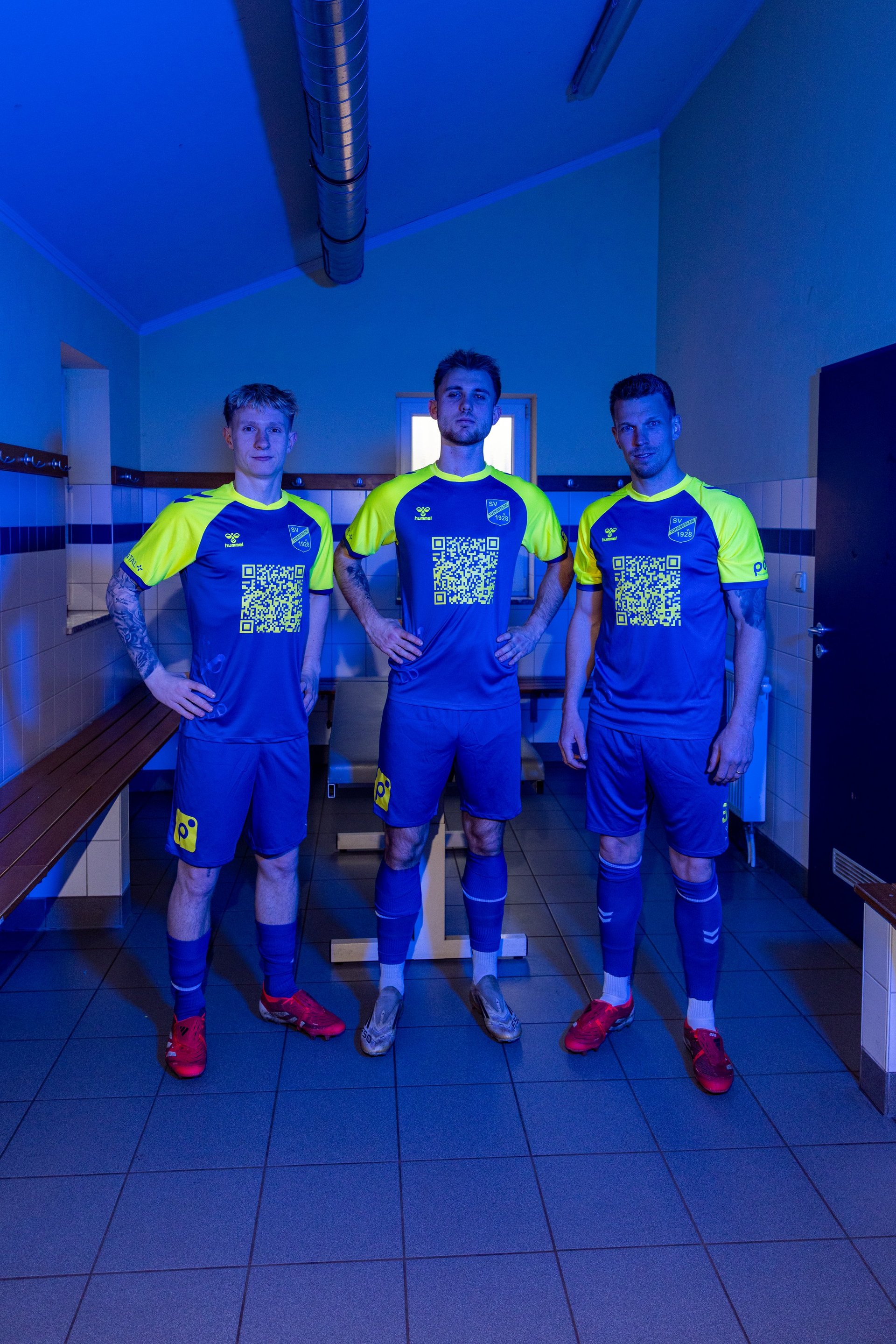 Three soccer players in blue and neon yellow uniforms with QR codes standing in a locker room